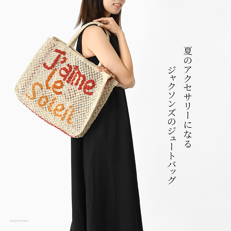 夏のアクセサリーになるジャクソンズのジュートバッグ。ナチュラルなジュート素材に鮮やかなカラーが映え、リゾートのような抜け感と高揚感を添えてくれる大容量トートバッグを肩掛けして歩く女性